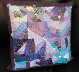 A patchwork pillow in shades of purple, embellished with buttons and beads.