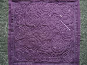 Purple fabric showing many lines of spiral stitching in a lighter (contrasting) shade of purple.